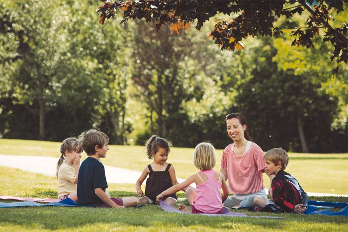 Happy children's yoga teacher with students in a park.